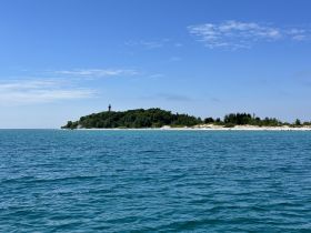 A stunning view of a serene coastline featuring a lighthouse, surrounded by clear turquoise waters — perfect for showcasing beautiful destinations on a boating trip.