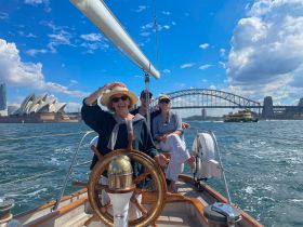 A joyful group sails through Sydney Harbour, with iconic landmarks like the Opera House and Harbour Bridge in the background, perfect for memorable sailing experiences.