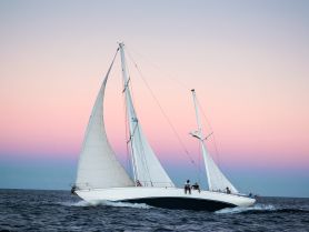 A beautiful sailboat glides through the water at sunset, with guests enjoying the serene atmosphere — perfect for a memorable sailing experience.