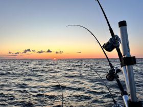 A serene sunset view over the ocean with fishing rods in the foreground, capturing the essence of a peaceful fishing trip at dusk.
