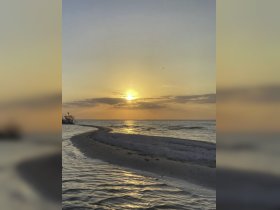 A stunning sunset casts golden hues over the tranquil coastline, creating a picturesque scene perfect for romantic getaways or peaceful retreats by the water.