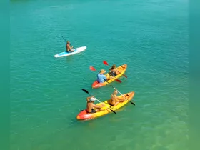 A vibrant scene of a group enjoying kayaking and paddleboarding in crystal-clear waters, perfect for adventure seekers and water sports enthusiasts.