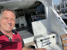 A man smiles for a selfie inside the cabin of a boat, showcasing the spacious interior and seating area, perfect for relaxing during a day on the water.