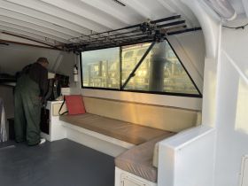 An interior view of a boat's cabin featuring a seating area and fishing rods, with a person preparing equipment. Ideal for fishing trips or relaxing onboard.