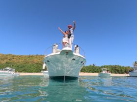 A couple celebrates on the bow of a boat, enjoying a sunny day at the beach — perfect for memorable moments and fun on the water.