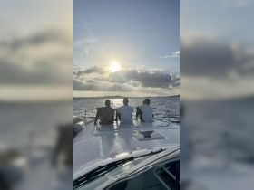A group of friends relaxes on the bow of a boat, enjoying a stunning sunset over the water — a perfect moment for camaraderie and tranquility on the sea.