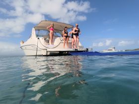 A group of friends enjoys a fun day on the water, preparing to dive off the back of their boat into the clear blue sea — perfect for summer adventures.