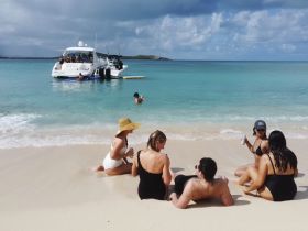 A lively group enjoys a beach day with drinks and fun in the sun, while a pontoon boat is anchored nearby, creating the perfect backdrop for a memorable outing.