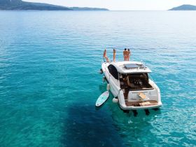 A lively group enjoys a sunny day on a boat, with some relaxing on deck and others in the crystal-clear turquoise waters — perfect for summer adventures.