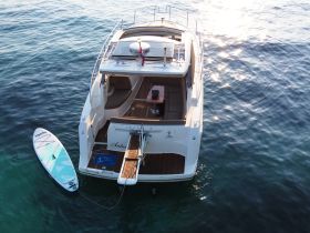 Aerial view of a sleek yacht anchored in clear waters, showcasing its elegant design and a paddleboard ready for adventure.