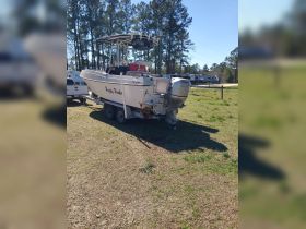 A well-maintained fishing boat named 'Happy Hooker' is parked on its trailer in a grassy area, showcasing its sleek design and readiness for the water.