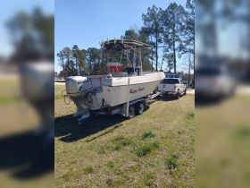 A side view of the 'Happy Hunter' boat, showcasing its sleek design while docked on a trailer, surrounded by lush greenery.