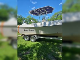 A side view of the 'Happy Hooker' boat on its trailer, showcasing its sleek design against a backdrop of greenery.
