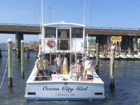 A group of friends prepares for a fishing trip aboard the 'Ocean City Girl' at the dock, showcasing camaraderie and excitement for a day on the water.