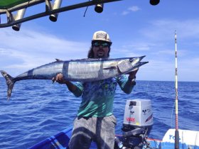 A proud angler holds up a large wahoo catch while fishing in the open ocean — a thrilling moment for any fishing enthusiast.