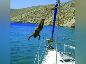 A man leaps off the side of a sailboat into the vibrant blue waters, capturing the thrill of summer adventures on the water.