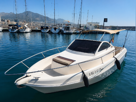 A sleek yacht docked in a marina, showcasing its elegant design against a backdrop of mountains and clear blue waters.