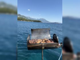 A close-up of a grill on a boat, sizzling with delicious meats, perfect for a barbecue experience on the water surrounded by stunning scenery.