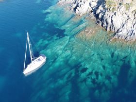 A stunning aerial view of a sailboat navigating through crystal-clear waters, showcasing the vibrant underwater scenery and rocky coastline.