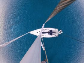 A stunning aerial view of a sailboat navigating through crystal-clear waters, showcasing its sleek design and the beauty of the open sea.