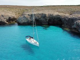 A stunning aerial view of a sailboat navigating through crystal-clear turquoise waters, surrounded by rocky cliffs — an ideal scene for sailing enthusiasts and nature lovers.
