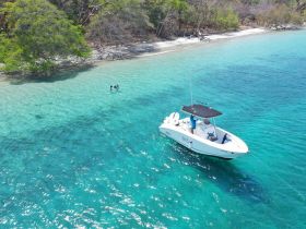 Aerial view of a boat anchored in crystal-clear turquoise waters, with two people enjoying a swim nearby — a perfect scene for a tropical getaway.