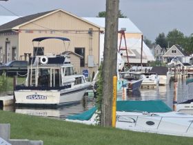 A well-detailed view of a docked boat named 'Lifesavers' at a marina, surrounded by other vessels and a picturesque waterfront setting.