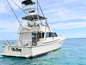 A stunning view of the 'Oh Boy' yacht cruising through clear waters, showcasing its sleek design and fishing equipment — perfect for deep-sea adventures.