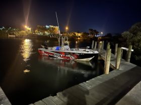 A sleek speedboat docked at night, illuminated by surrounding lights, showcasing its vibrant design against the calm waters.