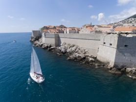 A picturesque sailing scene near historic fortifications, showcasing a sailboat navigating the clear waters against a backdrop of charming coastal architecture.