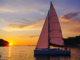 A beautiful sailboat with pink sails glides across the water at sunset, creating a picturesque scene perfect for romantic evening cruises.