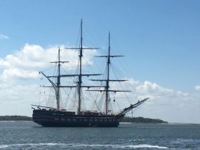 A majestic sailing ship navigates through calm waters, showcasing its impressive masts and sails against a clear blue sky — a perfect sight for maritime enthusiasts.