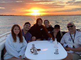 A joyful group enjoys a sunset cruise on a boat, sharing drinks and laughter as the sun sets over the water — perfect for family gatherings and celebrations.