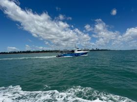 A speedboat glides through the turquoise waters, showcasing its sleek design against a backdrop of clouds and distant shoreline — perfect for thrilling water adventures.