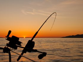 A serene sunset view from a fishing boat, showcasing the fishing rod silhouetted against the vibrant sky — perfect for capturing the tranquility of a day on the water.