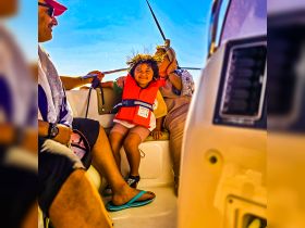 A joyful child in a life jacket smiles while sitting on a boat with family, capturing a moment of fun and safety on the water.