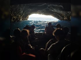 A group of adventurers enjoys a boat ride through a stunning cave, with the ocean visible in the background — a perfect setting for exploring natural wonders.