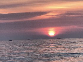 A stunning sunset over the ocean, with silhouettes of boats dotting the horizon — a picturesque moment perfect for evening cruises.