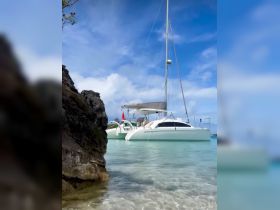 A serene view of a catamaran docked in crystal-clear waters, framed by rocky shores and a beautiful sky — perfect for exploring tropical destinations.
