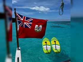 Two bright paddleboards are anchored in crystal-clear waters, with a Bermuda flag waving in the breeze — perfect for a day of fun on the water.