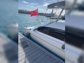 A close-up view of a catamaran docked with a flag waving in the breeze, showcasing the sleek design and tranquil marina setting.