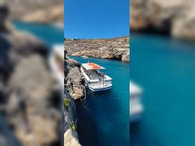A picturesque view of the 'Julie' boat docked in a serene cove, surrounded by rocky cliffs and clear blue waters, perfect for a relaxing day on the water.