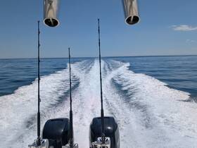 A view from the back of a boat showcasing fishing rods and the wake created as it moves through calm waters, perfect for fishing enthusiasts.