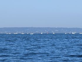 A distant view of multiple boats on the water, with a hazy background, making it difficult to discern details.