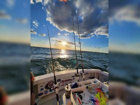 Fishing gear is set up on the boat as the sun sets over the water, creating a picturesque backdrop for a day of fishing adventures.