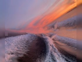 A visually distorted image of water and sky, creating an abstract representation of a boating experience at sunset.