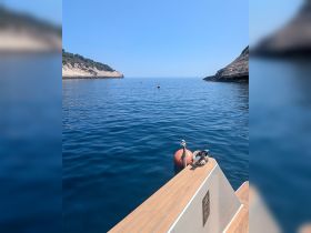 A serene view from the bow of a boat, showcasing calm waters and rocky cliffs in the distance — perfect for tranquil boating experiences.