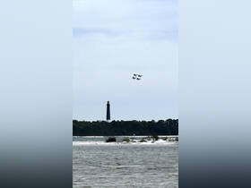 A stunning view of a lighthouse with jets performing an airshow above, capturing a perfect blend of maritime and aerial excitement.