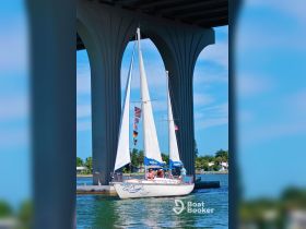 A sailing boat named 'Phoenix' navigates under a bridge, showcasing a group enjoying their time on the water — a perfect scene for sailing enthusiasts.