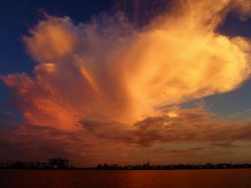 A stunning display of clouds at sunset, creating a vibrant sky over the water. Ideal for capturing the beauty of nature.